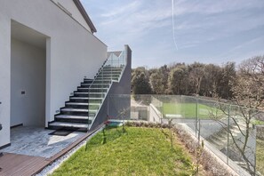 Stairs lead to an upper level, flanked by a white exterior wall and a small outdoor area with a deck and lawn.