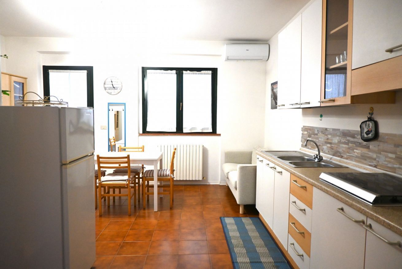 Eine kompakte Küche mit Kühlschrank, Esstisch, Stühlen, Spüle und Schränken.