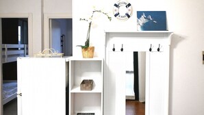 Una habitación con una cama litera, un armario blanco con estantes, una cesta de mimbre, un cartel de bienvenida y un cuadro enmarcado.