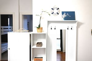 Une chambre avec un lit superposé, une armoire blanche avec des étagères, un panier en osier, une pancarte de bienvenue et un tableau encadré.