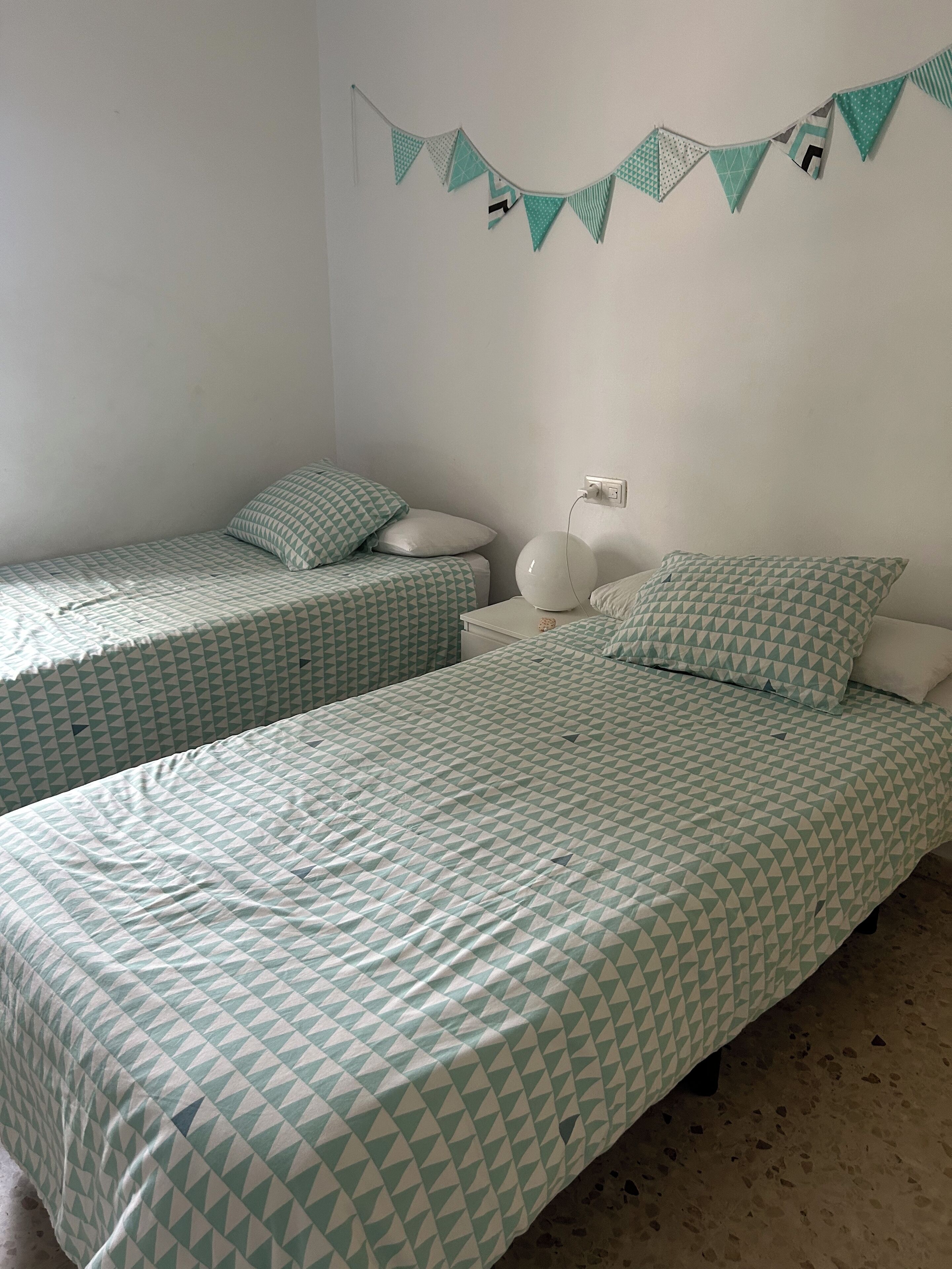 Une chambre avec deux lits simples, chacun agrémenté d’une literie à motifs, une table de chevet avec une lampe et un luminaire fixé au mur.