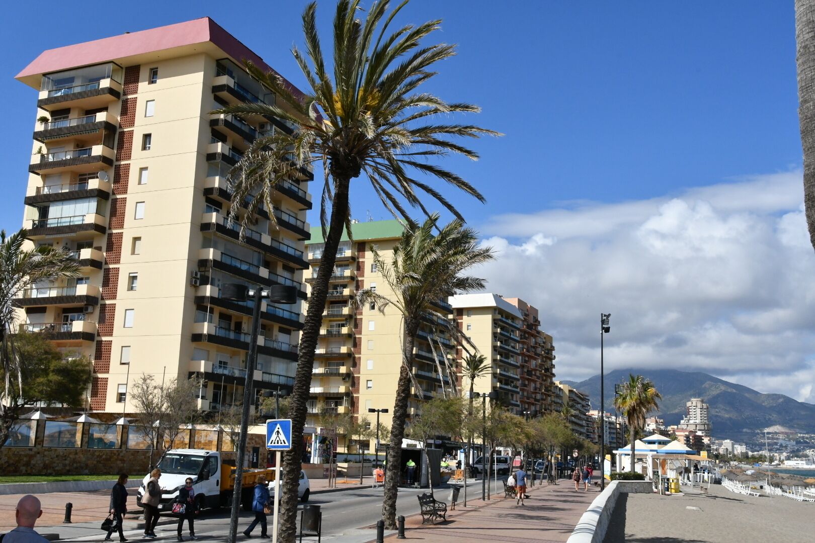 Un edificio residencial de varios pisos con balcones, palmeras y una acera.