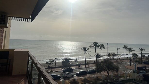 A balcony with a view of the sea, palm trees, and parked cars. - Nice apartment, in front of the beach. (Fuengirola)