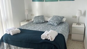 A neatly made bed with patterned bedding, two bedside tables with lamps, and a wall with three paintings. - Nice apartment, in front of the beach. (Fuengirola)