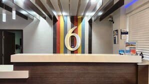 A reception desk with a large number '6' sign, a colorfully tiled wall, and a security camera.