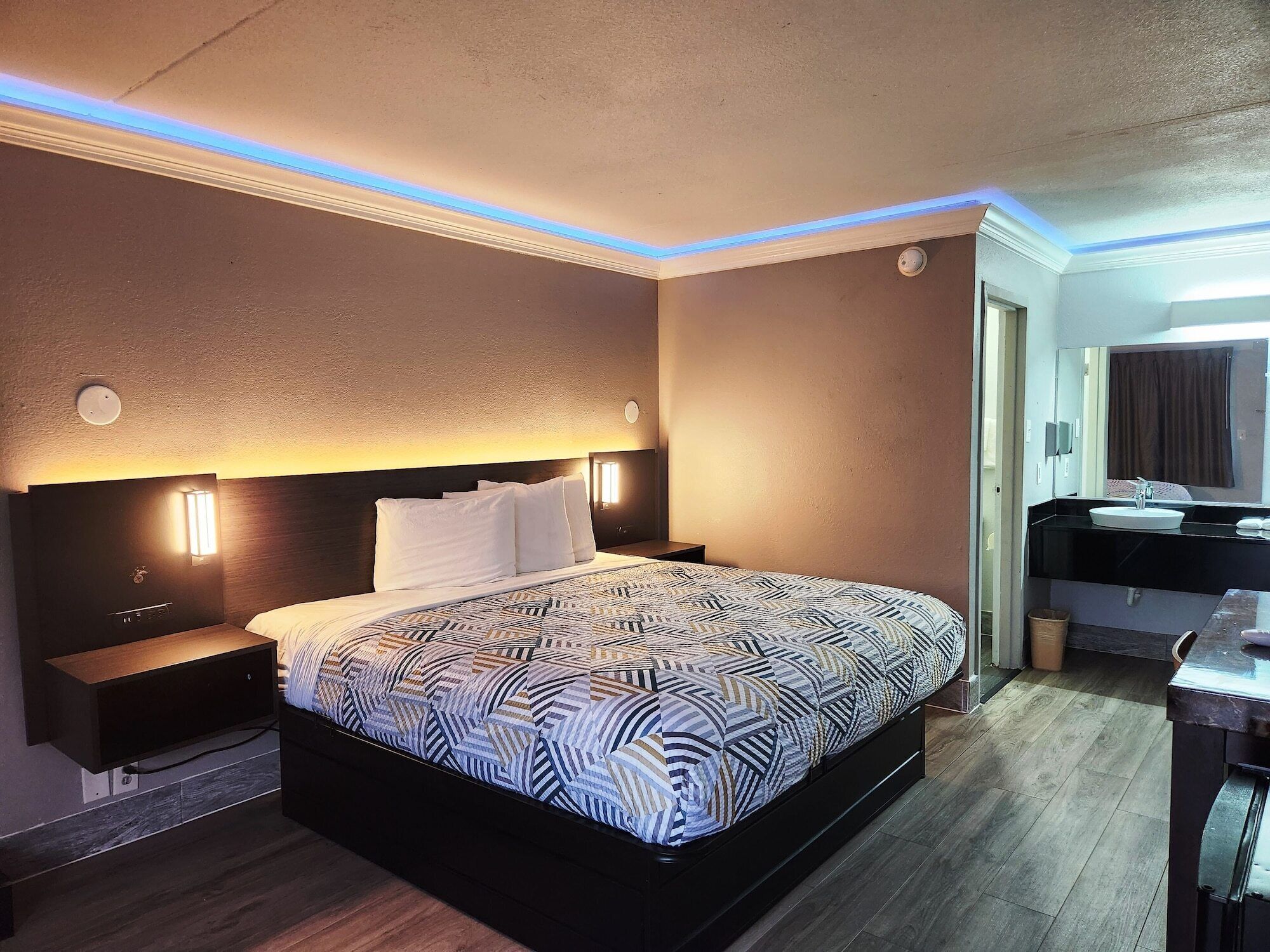 Habitació d'hotel amb un llit gran, taules de nit, escriptori i un bany amb un lavabo i mirall.