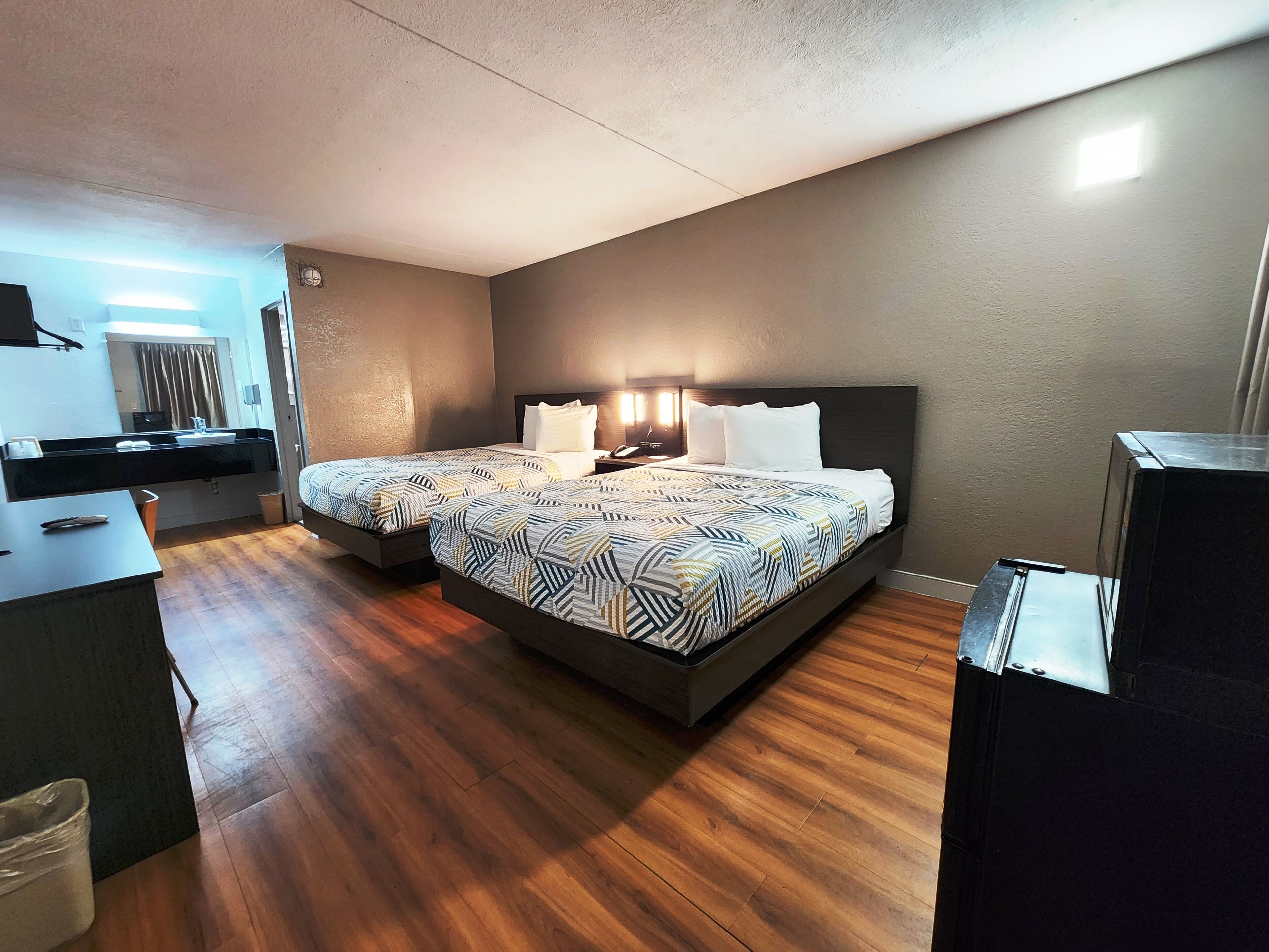 Una habitación de hotel moderna con una cama grande, mesitas de noche, un escritorio y un baño a la vista a través de una puerta abierta.