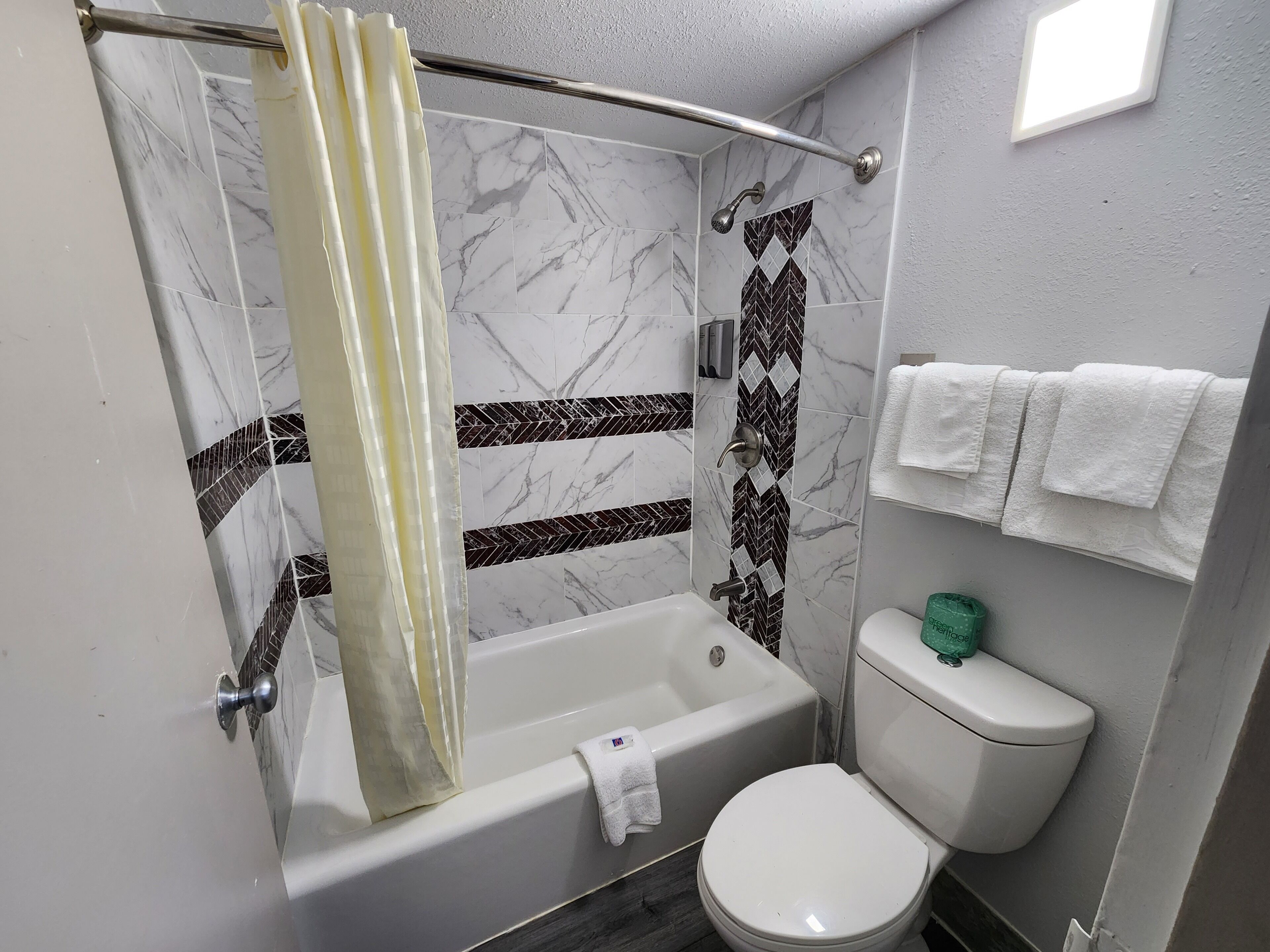 A bathroom with a shower, bathtub, toilet, and a towel rack with multiple towels.