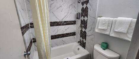 A bathroom with a shower, bathtub, toilet, and a towel rack with multiple towels.