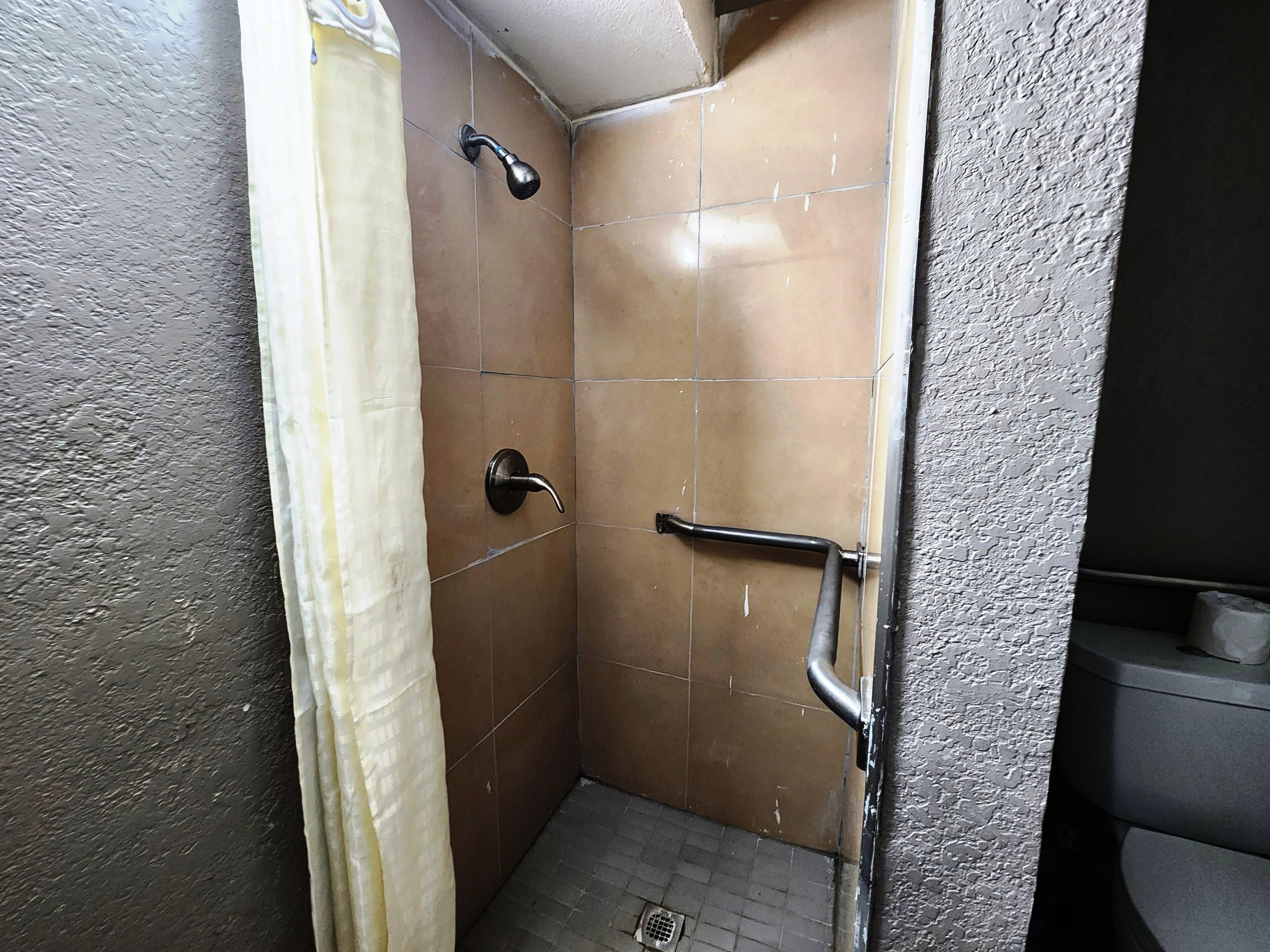 A small, tiled shower area with a showerhead, a grab bar, and a curtain.
