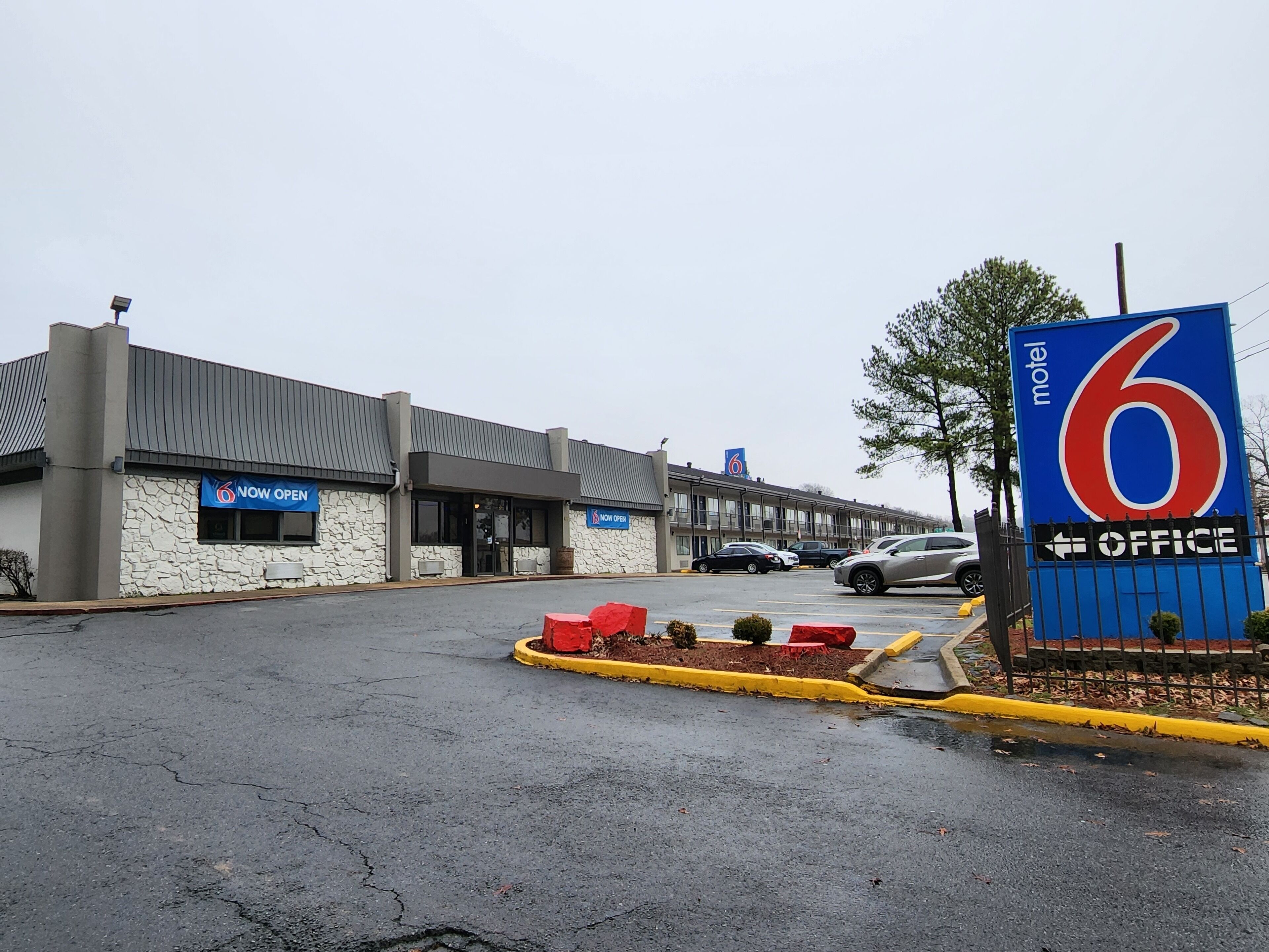 Un motel avec une façade en pierre, une enseigne avec le chiffre « 6 » et une autre indiquant « OUVERT MAINTENANT ».