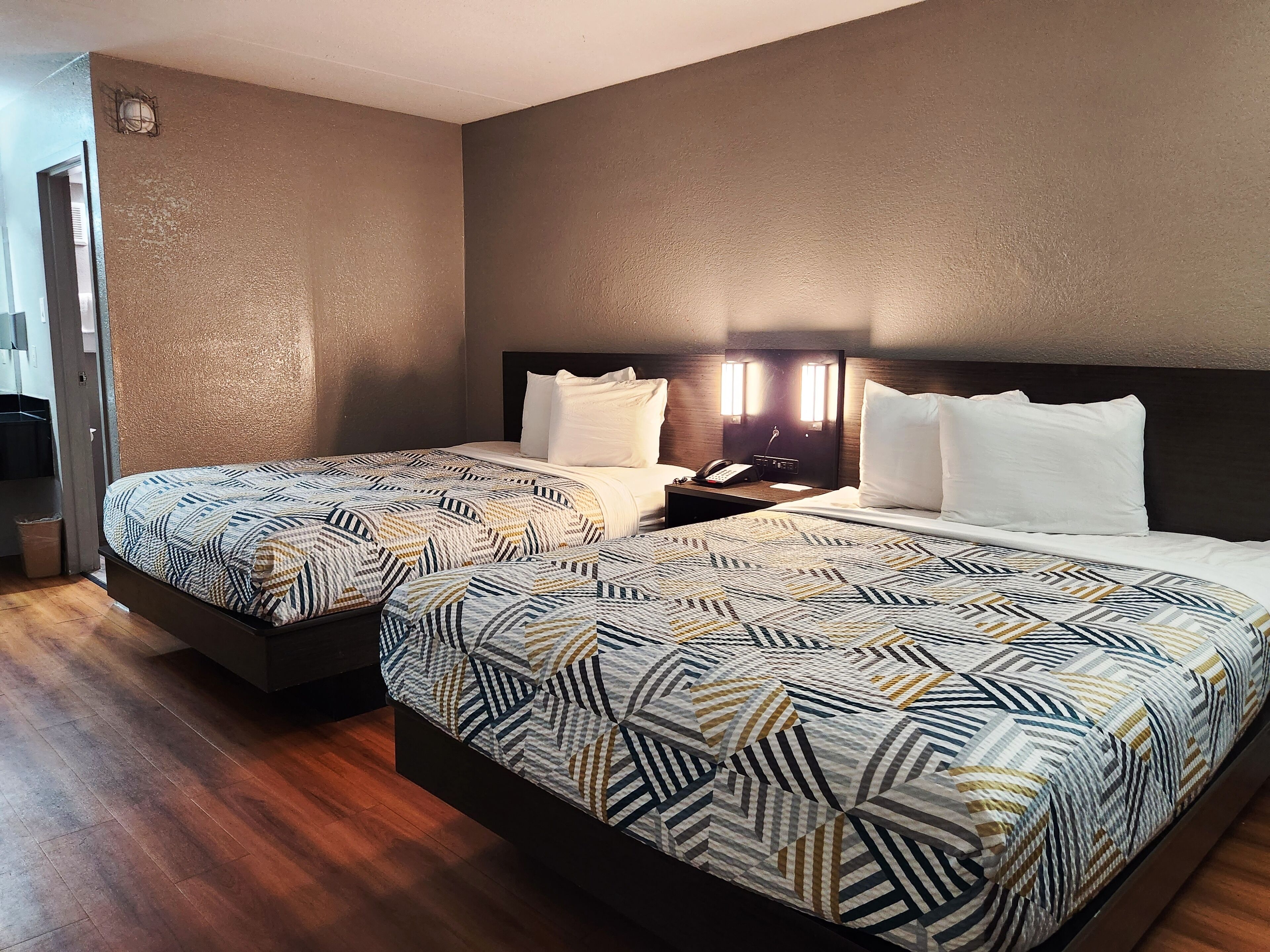 Habitación de hotel con dos camas, piso de madera, cabecera oscura y mesita de noche con un teléfono.