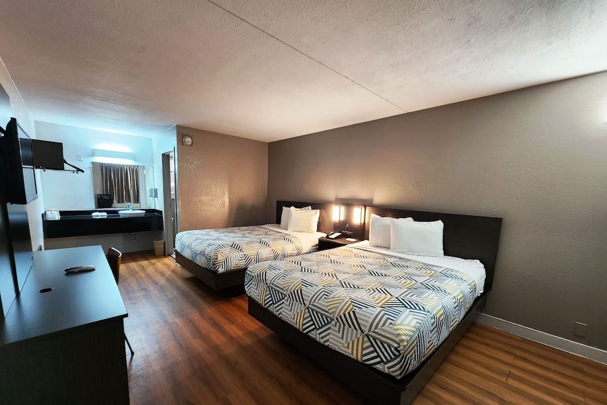 A hotel room with two beds, a desk, a mirror, and a bathroom visible through an open door.