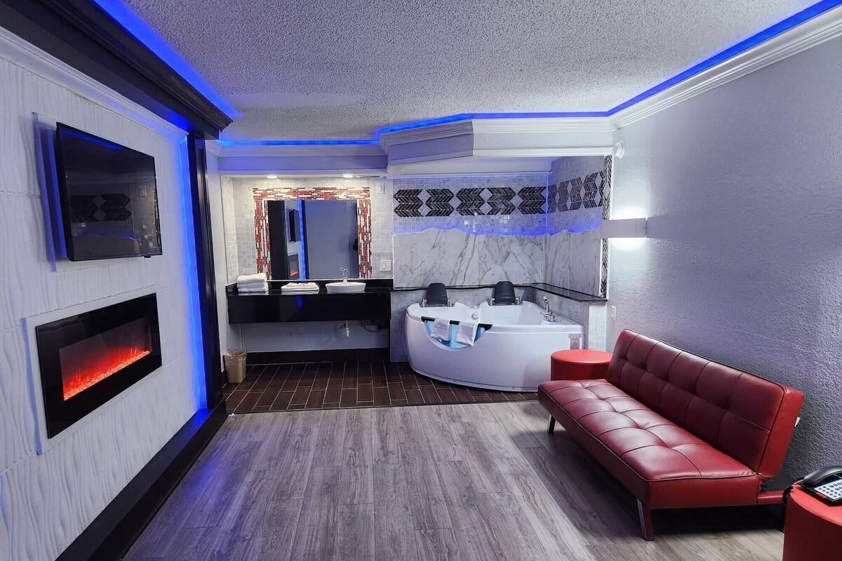 A modern bathroom with a built-in jacuzzi, a red leather bench, and a TV mounted on the wall.