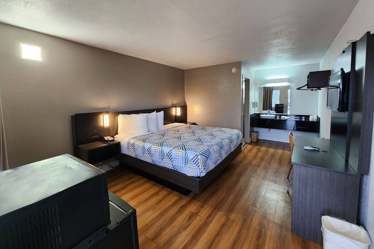 A hotel room with a bed, bedside table, lamp, and a small desk with a chair.