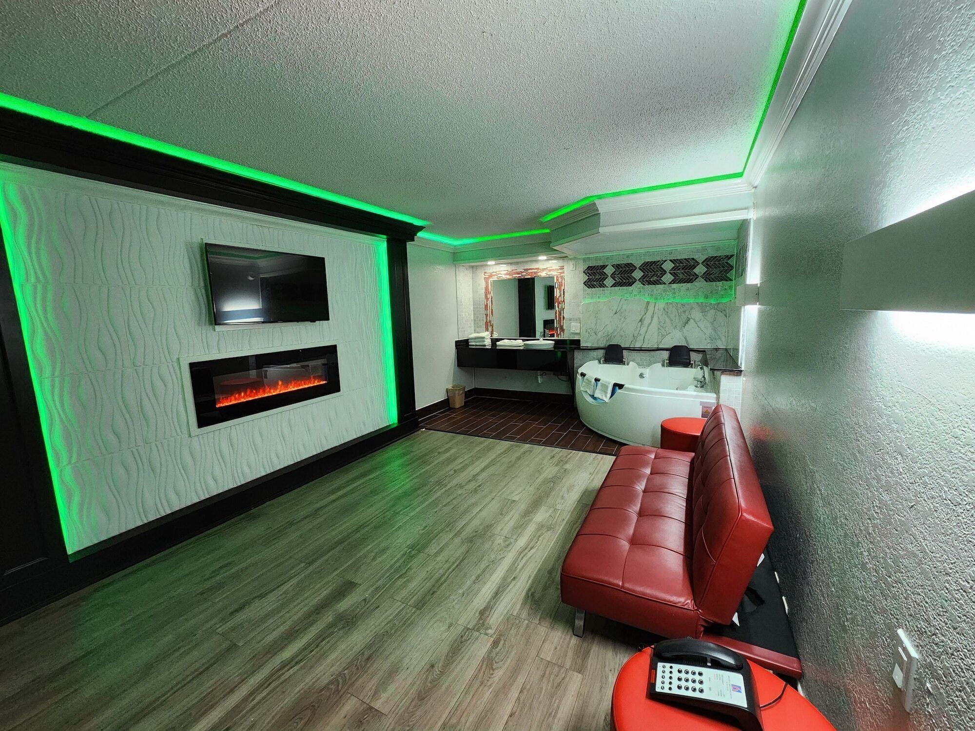 Un baño moderno con bañera, un banco rojo y televisor montado en la pared.