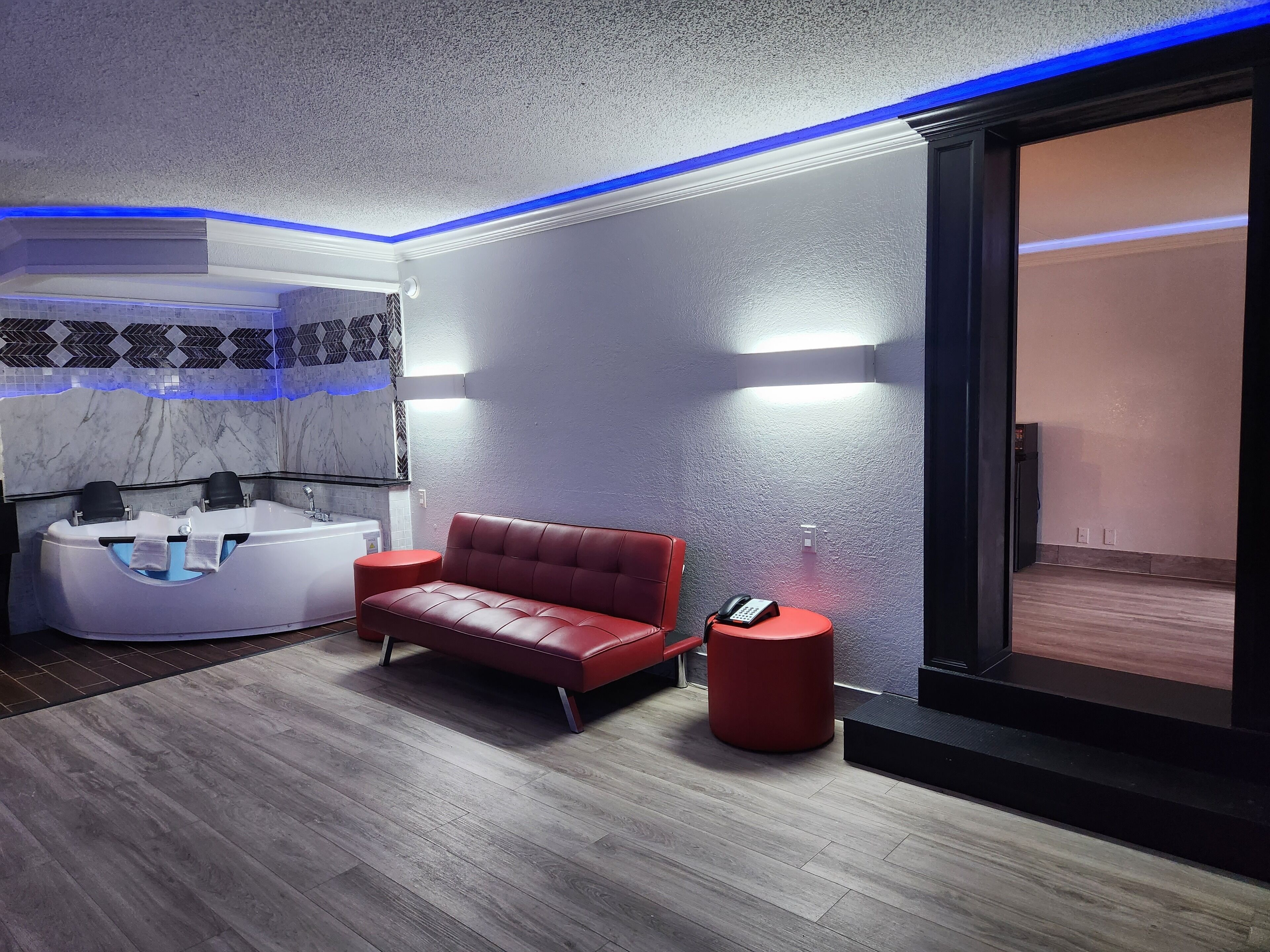 A modern spa room with a red leather sofa, a white massage chair, and a red stool.