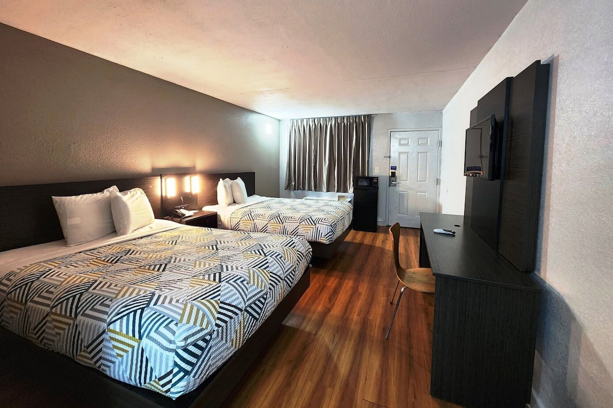 A hotel room with two beds, a desk, a TV, and a door.