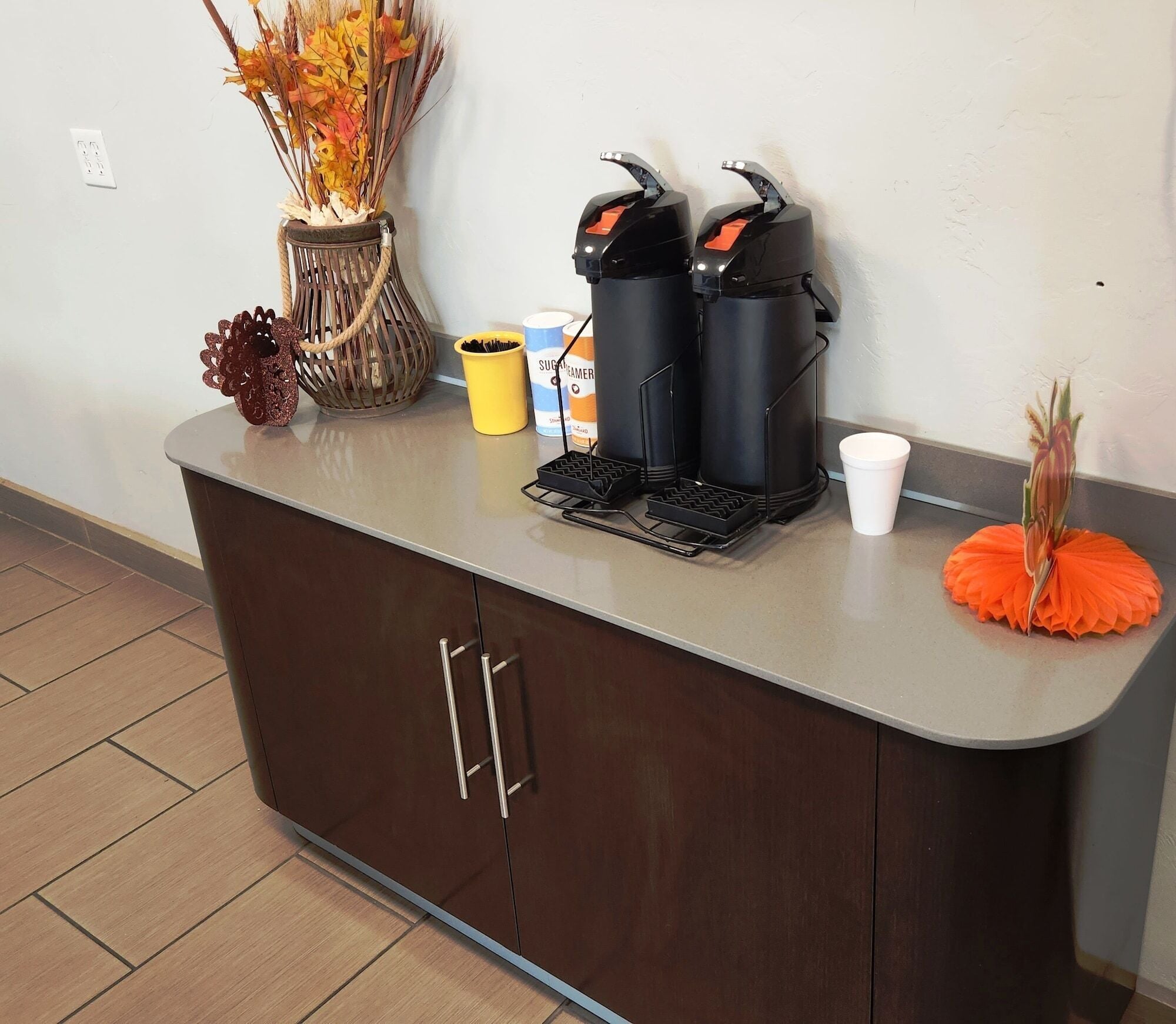 A kitchen counter with a coffee maker, a sugar container, a white cup, and decorative items.
