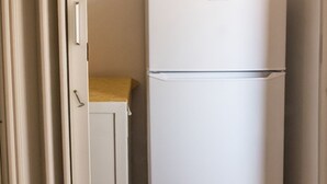 Un refrigerador blanco en un pasillo estrecho, con una puerta a la izquierda y un armario a la derecha.