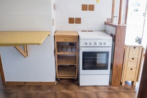 A kitchen with a white stove, wooden shelves, and a wooden table.