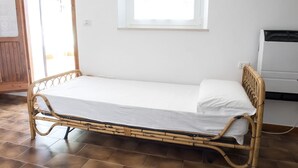 Una cama individual con colchón blanco y estructura de madera en una habitación con suelo de baldosas y ventana.