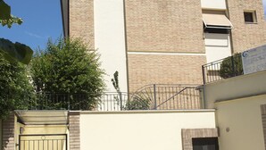 Un edificio de varios pisos con fachada de ladrillo, entrada con portón y un pequeño balcón con barandilla de metal.