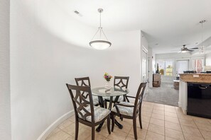 A dining area with a glass table and dark wooden chairs, a ceiling fan, and a kitchen visible in the background. - Sunset Sound: Water Views, Shared Pool, Elevator (Nags Head)