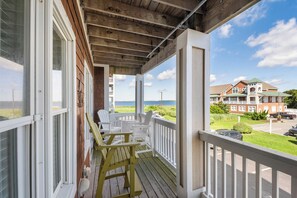 A wooden deck with white railings and chairs, overlooking a beach and a large house. - Sunset Sound: Water Views, Shared Pool, Elevator (Nags Head)