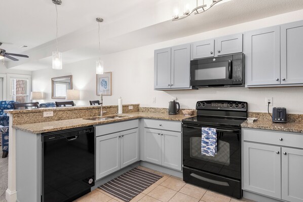A modern kitchen with grey cabinets, a black stove, a microwave, and a dishwasher. - Sunset Sound: Water Views, Shared Pool, Elevator (Nags Head)