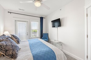 A bedroom with a bed, a ceiling fan, a TV, a chair, and a window with blinds. - Sunset Sound: Water Views, Shared Pool, Elevator (Nags Head)