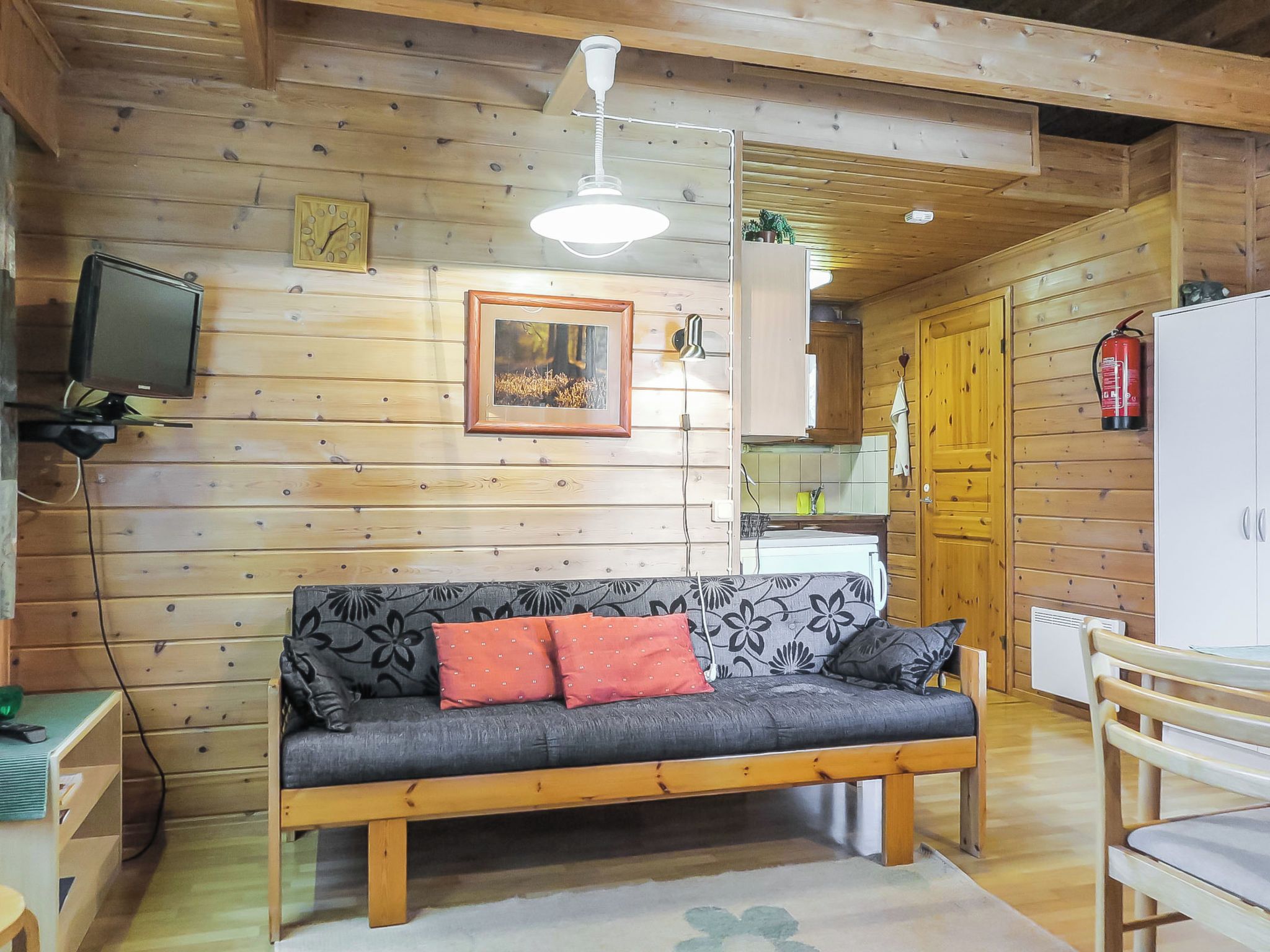 A cozy cabin interior with a wooden sofa, a television, a framed picture, and a kitchen area.