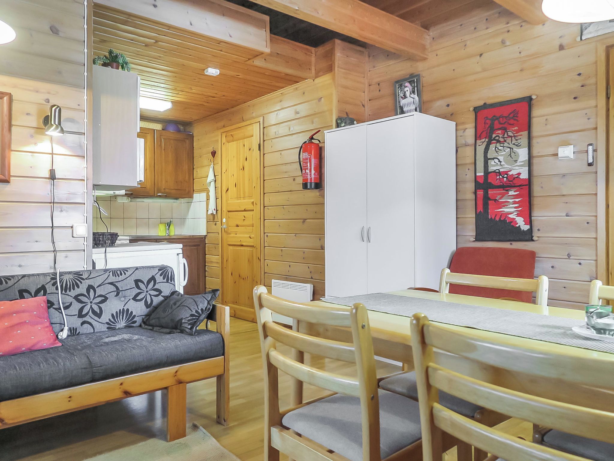 Un interior cálido de cabaña con sofá, mesa de comedor, sillas, paredes de madera y una zona de cocina.