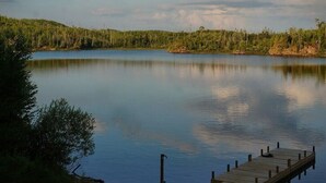 Un lac paisible avec une jetée en bois qui s’avance sur l’eau, entouré d’une forêt dense.