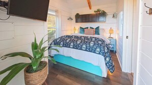 Un dormitorio con una cama, un ventilador de techo, un televisor montado en la pared y una planta en maceta.