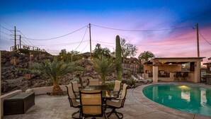 Zona de piscina con mesa y sillas, rodeada de cactus y palmeras.