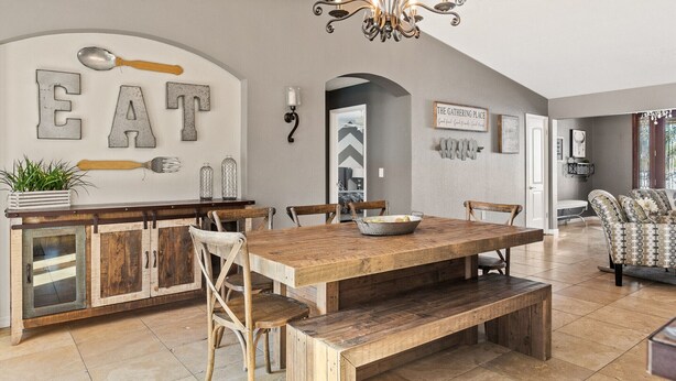 Un comedor con una mesa de madera y bancos, una isla de cocina con decoración de cuchara y tenedor, y una araña.
