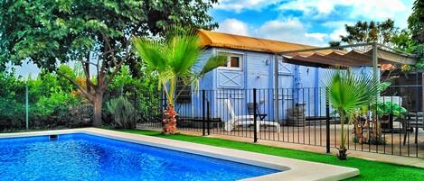 A swimming pool with a blue tiled edge, surrounded by a green lawn and a fence.