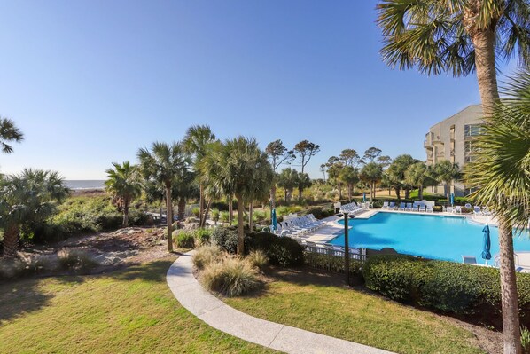 A pool area with lounge chairs and palm trees, surrounded by a landscaped garden and a building in the background.