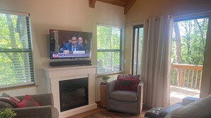 Ein Wohnzimmer mit Kamin, Fernseher und Blick ins Freie.