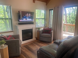 Ein Wohnzimmer mit Kamin, Fernseher und Blick ins Freie.