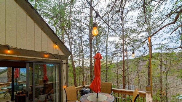Eine Terrasse im Freien mit einem runden Tisch, Stühlen, einem roten Sonnenschirm und hängenden Lampen.