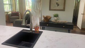 Eine Küche mit modernem Spülbecken, ein Essbereich mit Tisch und Stühlen, ein gerahmtes Kunstwerk an der Wand und Blick ins Freie.