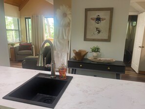 A kitchen with a modern sink, a dining area with a table and chairs, a framed artwork on the wall, and a view of the outdoors. - Helen Hideaway| 2 BR| Golf Community and Amenities (Helen)