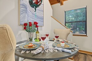 A round dining table with a lace table runner, a vase with red roses, a bottle of wine, and two glasses of red wine. - The Nest at Innsbruck| 2 BR| Golf Community and Amenities (Helen)