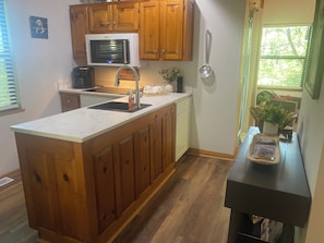 A kitchen with wooden cabinets, a microwave, a sink, and a window with a view of greenery. - Helen Hideaway| 2 BR| Golf Community and Amenities (Helen)