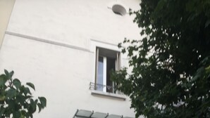 Un edificio con fachada blanca, un pequeño balcón con barandilla de metal y una ventana con vista al cielo.