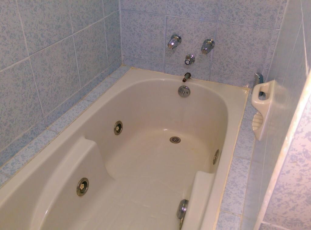 Una bañera blanca con desagüe, cabezal de ducha manual y grifo.