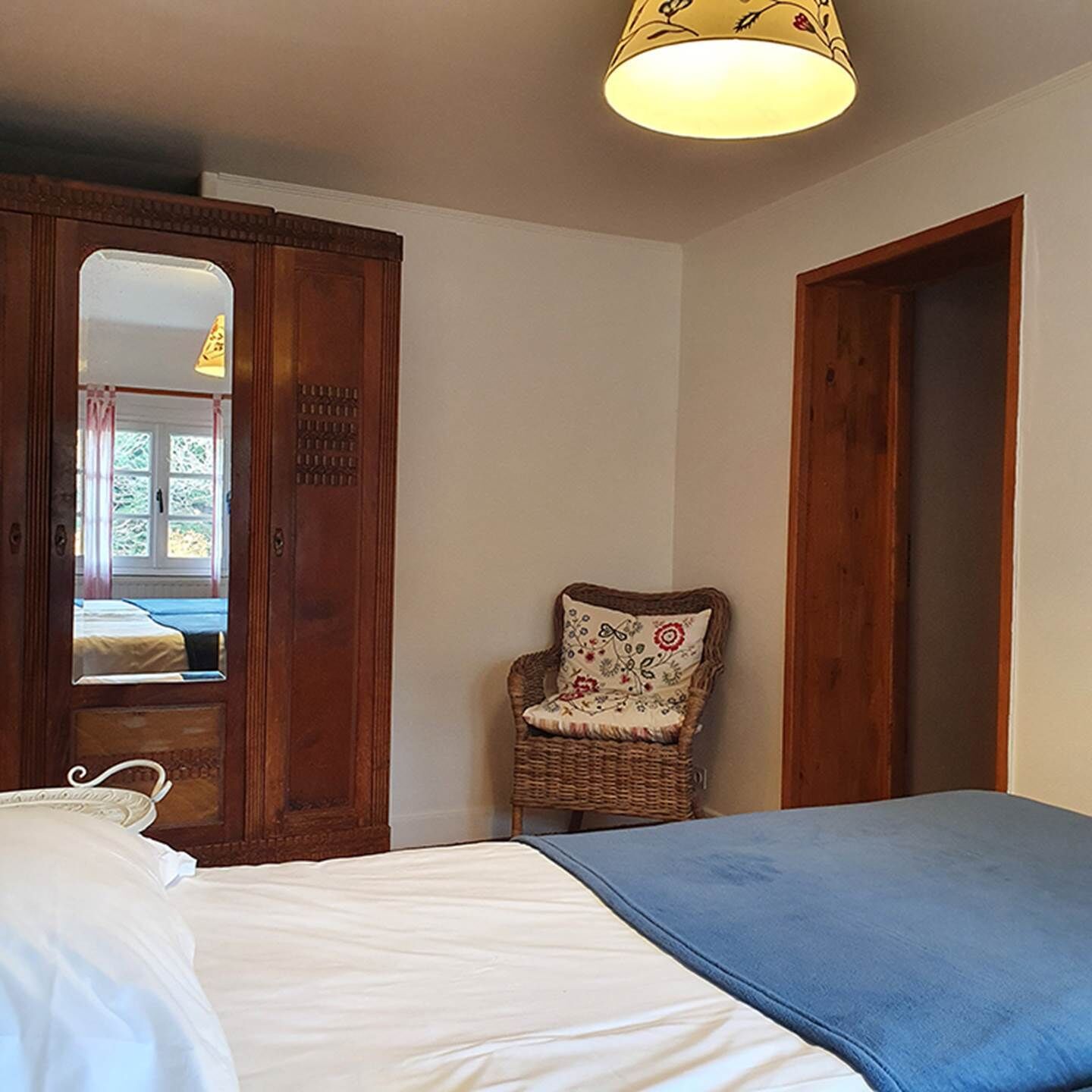 A bedroom with a bed, a chair, a wardrobe, and a mirror.
