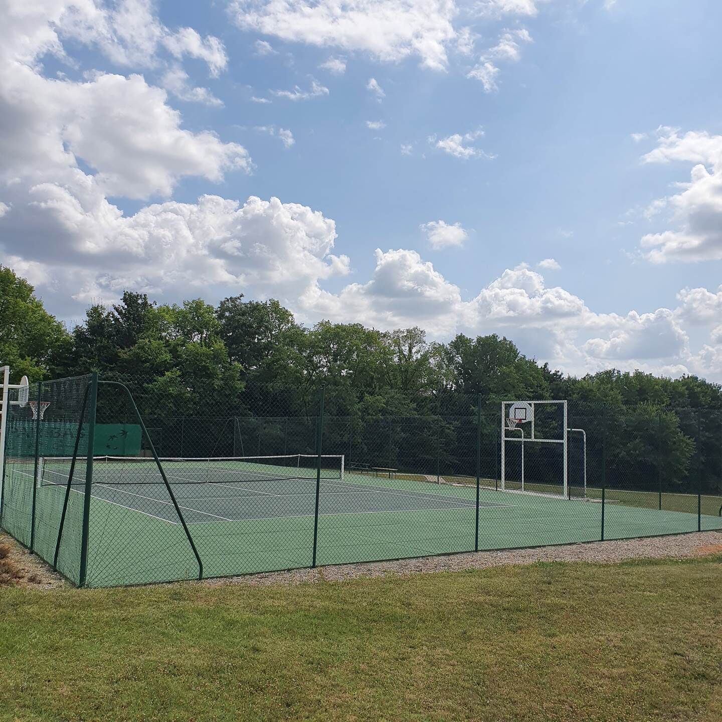 Un terrain de basket-ball en plein air, doté d’une surface verte, entouré d’une clôture grillagée et muni d’un panier de basket.